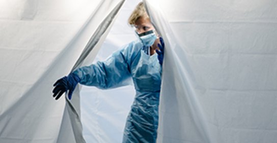 Nurse in full protective gear walking through the entrance of a tent