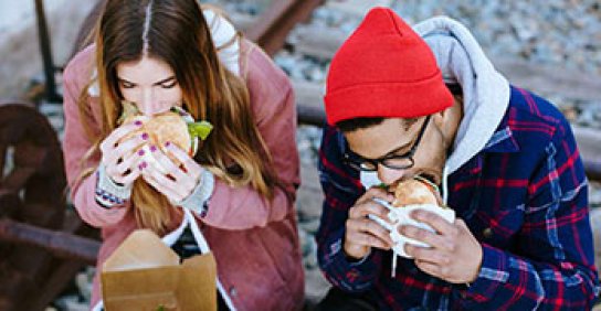 Male and female millennials sitting down and eating burgers